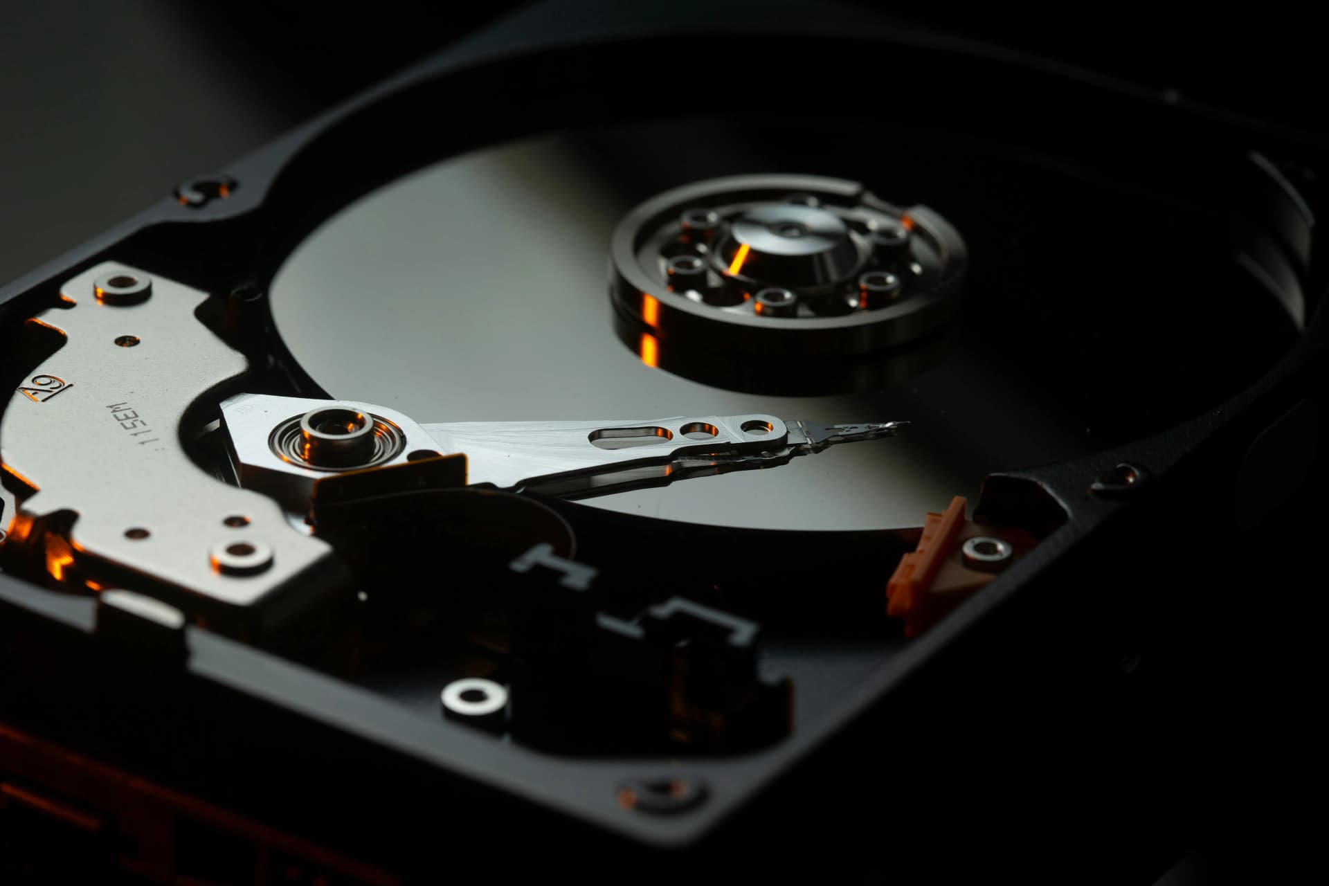 Close-up of an open hard disk drive showing its shiny platter, spindle, and read/write arm in low warm light